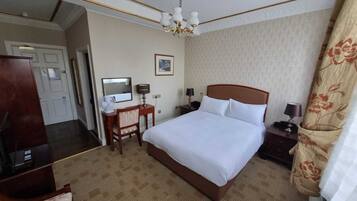 Hotellihuone, jossa on suuri sänky, työpöytä tuolilla, yöpöytä lampun kanssa, peili ja kattokruunu.