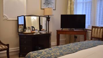 Una habitación de hotel con cama, escritorio con lámpara, televisor y cómoda.