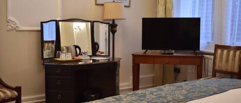 A hotel room with a bed, a desk with a lamp, a television, and a dresser.