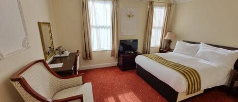 A hotel room with a bed, a desk with a chair, a television, and a mirror.