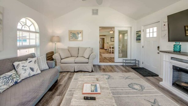 Ein geräumiges Wohnzimmer mit einer Couch, einem Couchtisch mit einem Buch, einem Kamin und einem Deckenventilator.