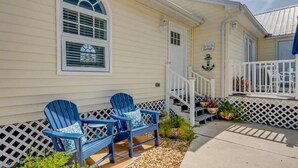 Ein Cottage mit Veranda, zwei Adirondack-Stühlen, einem Schild mit der Aufschrift 'Beach Cottage' und einer kleinen Treppe, die zum Eingang führt.