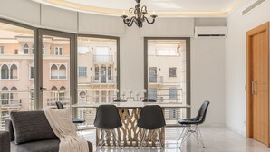 Uma sala de jantar moderna com uma mesa, cadeiras, janelas amplas e um lustre.