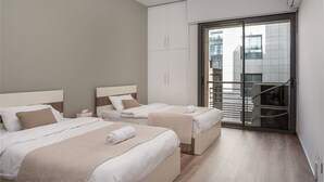 Quarto de hotel moderno com duas camas, uma janela grande e vista para a cidade.