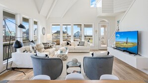 A spacious living room with a large window, a flat-screen TV, and a high ceiling. - #Beach Please - Amazing Views From All Directions - Close to the beach (Crystal Beach)