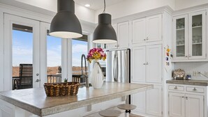 A modern kitchen with white cabinetry, a large island with stools, pendant lighting, and a view to the outdoors. - #Beach Please - Amazing Views From All Directions - Close to the beach (Crystal Beach)