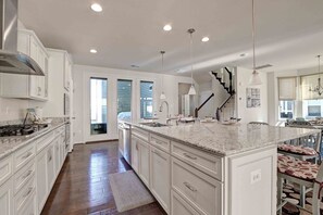 A spacious kitchen with white cabinetry, a large island, and a view of the living area.