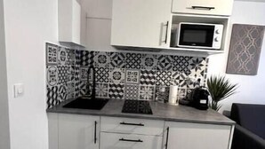 Une cuisine de taille réduite avec des meubles blancs, un four à micro-ondes et des carreaux décoratifs sur le mur derrière l’évier.