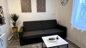 Un salon avec un canapé noir, une table basse blanche et deux horloges fixées au mur.