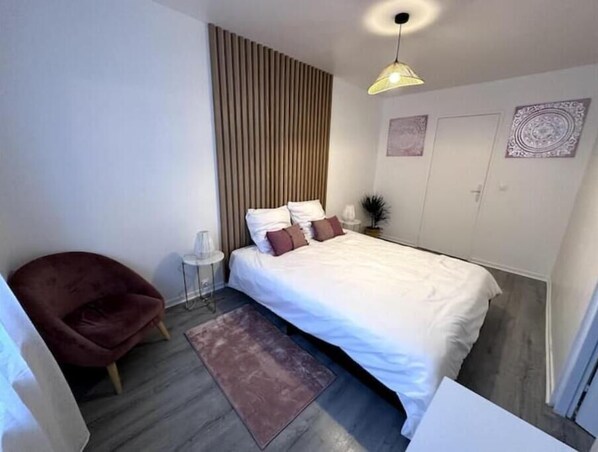 A modern bedroom with a bed, a chair, a small table, and a hanging light fixture.