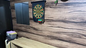 Ett rum med en väggpanel av trä, en darttavla, ett skrivbord med en fjärrkontroll och en hög med hopvikta handdukar.