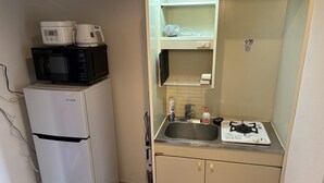 Ett litet, praktiskt kök med ett vitt kylskåp, en mikrovågsugn, ett litet handfat och en gasspis.