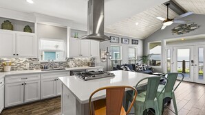 Uma cozinha moderna com armários brancos, uma ilha grande e um ventilador de teto.