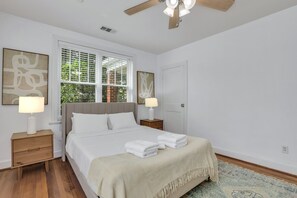 Quarto com cama, mesas de cabeceira, ventilador de teto e obras de arte nas paredes.