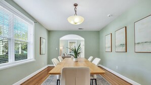 Ein Esszimmer mit Holztisch, weißen Stühlen, einem Blumentopf und gerahmten Bildern an den Wänden.