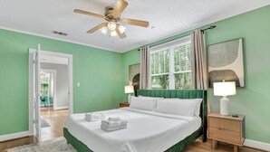 Ein Schlafzimmer mit einem großen Bett, einem Deckenventilator, einem Nachttisch und einem Fenster mit Vorhängen.