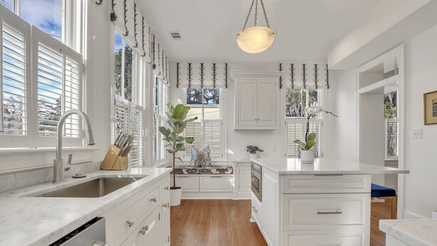 Une cuisine moderne avec des meubles blancs, un grand îlot central et un coin fenêtre aménagé en siège.