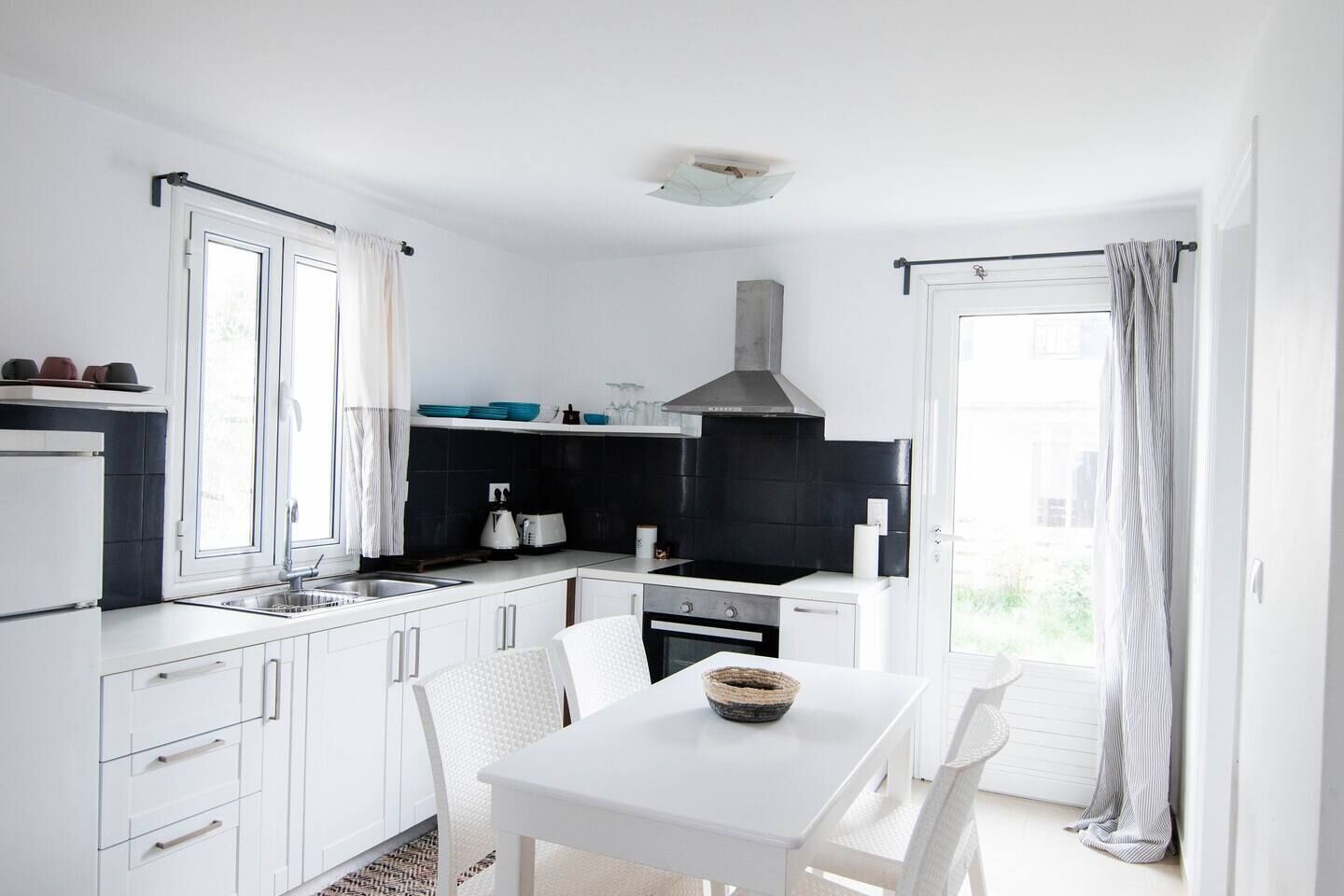 A modern kitchen with white cabinetry, a black backsplash, and a dining area with a white table and chairs.