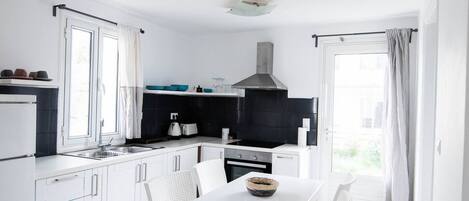 A modern kitchen with white cabinetry, a black backsplash, and a dining area with a white table and chairs.