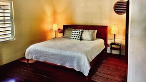 A bedroom with a bed, two bedside lamps, a window with blinds, and a circular wall decoration.