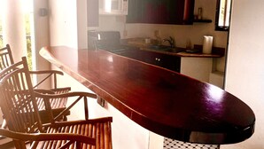 A kitchen with a wooden bar counter, chairs, a microwave, and cabinets.