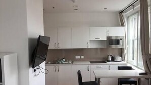 A modern kitchen with white cabinets, a microwave, and a sink. There is a dining area with a table and chairs. - Heart of Nottingham - turret studio (Nottingham)