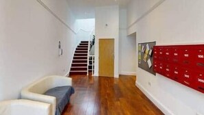 Un couloir avec un escalier, une rangée de boîtes aux lettres rouges et un mur blanc.