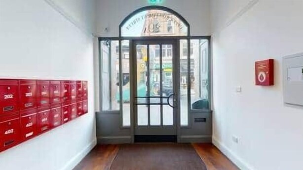 Un couloir avec un plancher en bois, une boîte aux lettres rouge et une porte dotée d’un panneau en verre.