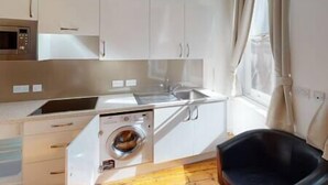 A compact kitchen with a built-in washing machine, a microwave, and a sink. - Quieter Studio for City Centre Location (Nottingham)