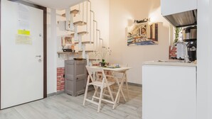 Une cuisine compacte avec un coin repas, un meuble blanc, un mur d’accent en briques et un tableau accroché au mur.
