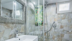 Une salle de bain dotée d’une douche à parois de verre, d’un lavabo blanc et de murs décorés d’un motif imitant la pierre.
