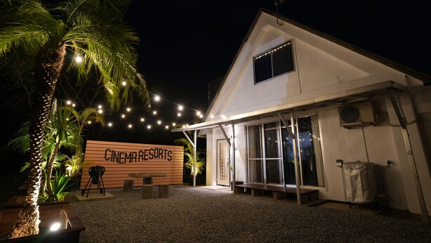 A building with a sign reading "CINEMARSETS" at night, featuring a covered outdoor seating area, palm trees, and string lights. - CINEMA RESORTS 4 (Motobu)