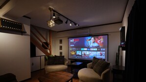 A living room with a large flat-screen TV, wooden flooring, and a staircase. - CINEMA RESORTS 4 (Motobu)