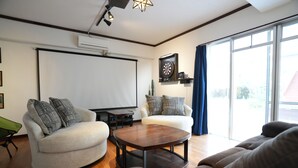 A living room with a large screen, two sofas, a coffee table, and a window with curtains. - CINEMA RESORTS 4 (Motobu)