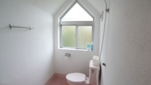 A small, white bathroom with a window, a toilet, and a shower area. - CINEMA RESORTS 4 (Motobu)