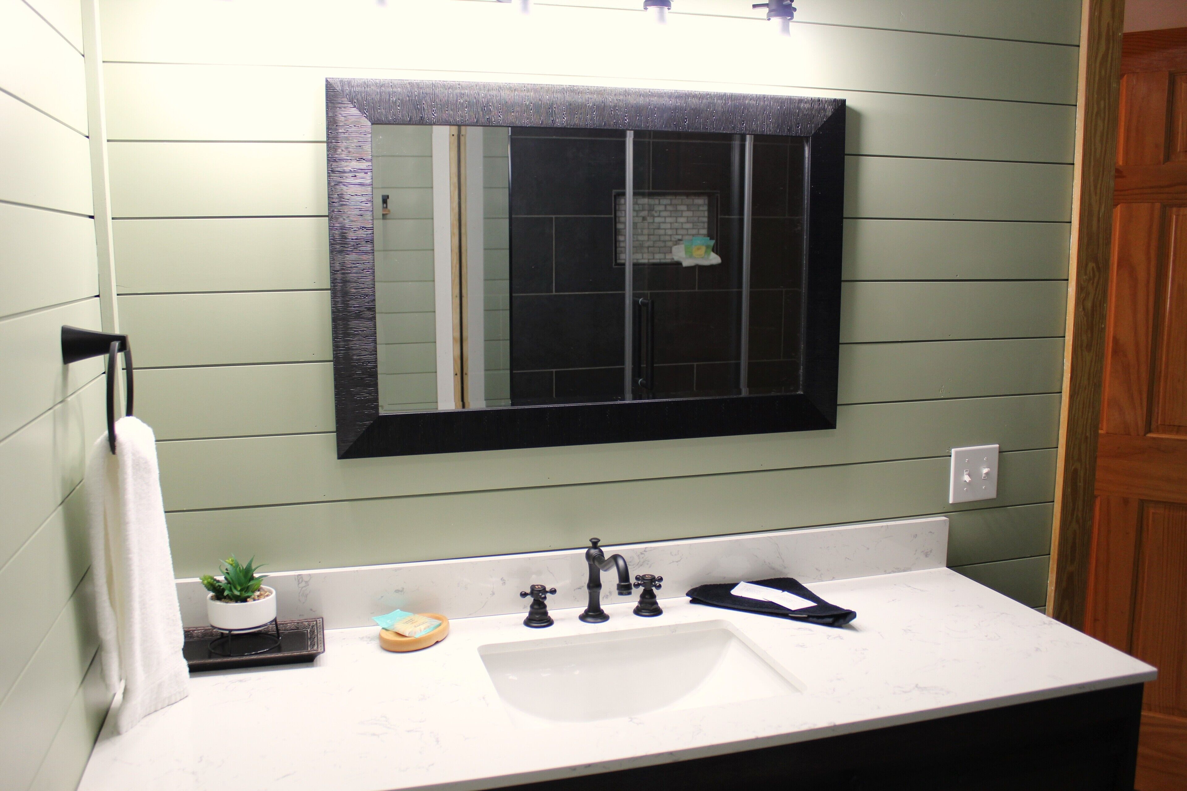 A bathroom with a white sink, a mirror, and a small potted plant on the counter.