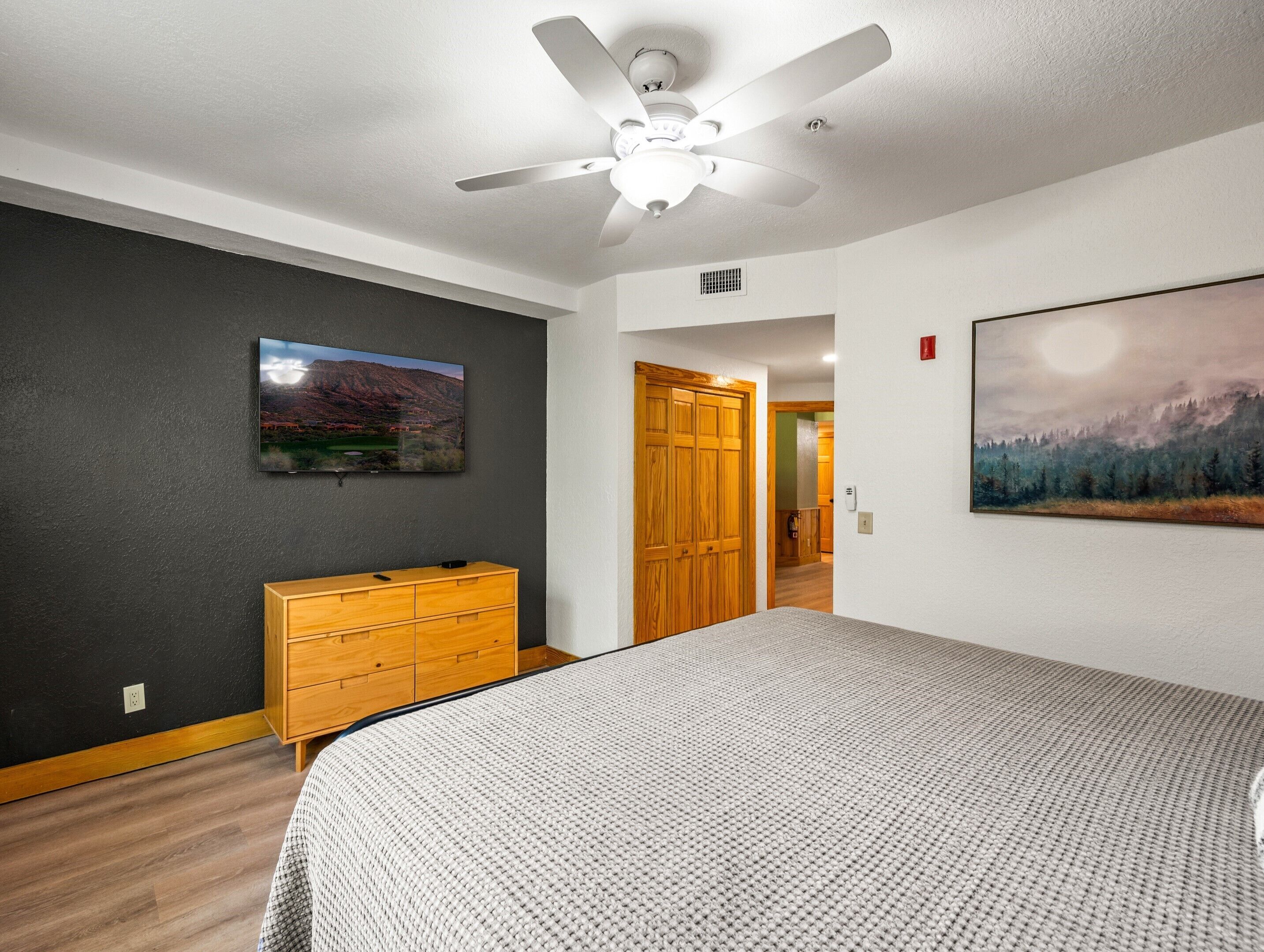 Ein Schlafzimmer mit Bett, Schminktisch, Deckenventilator, Fernseher und zwei Bildern.