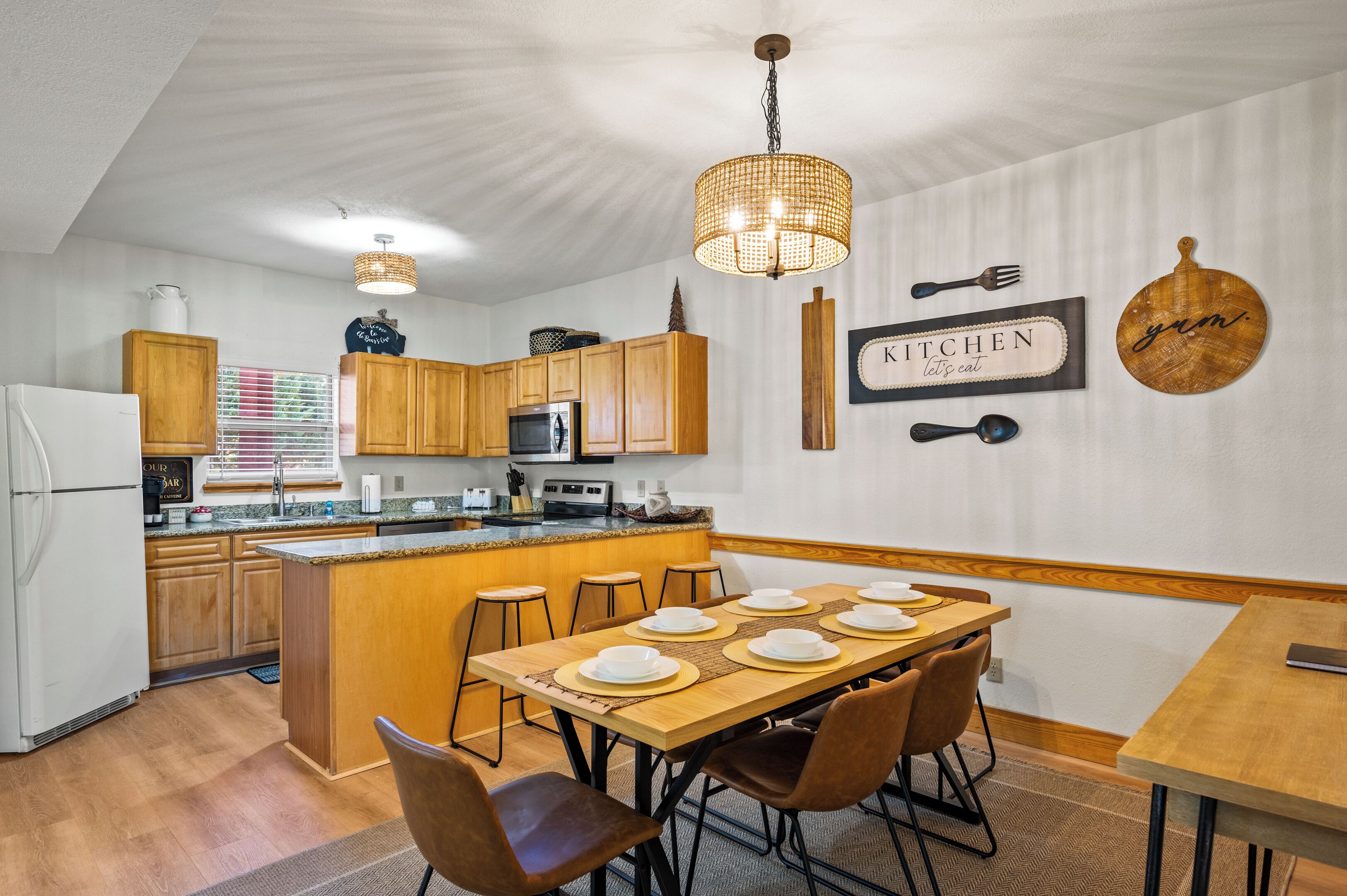 Cozinha moderna com armários de madeira, uma ilha central e uma área de jantar com mesa posta para seis pessoas.