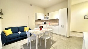 Un espace de vie compact comprenant un coin cuisine, un coin repas avec une table et des chaises, et un canapé avec des coussins.