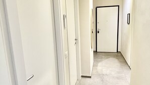 Un couloir aux murs et aux portes blancs, qui mène à une pièce dont la porte est noire.