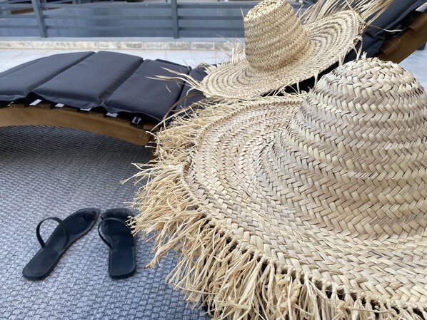 A wicker lounge chair with a woven hat and black flip-flops on a textured floor.