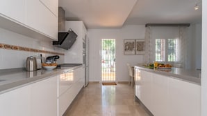 Une cuisine moderne avec des meubles blancs, des appareils en acier inoxydable et une vue sur l’extérieur.