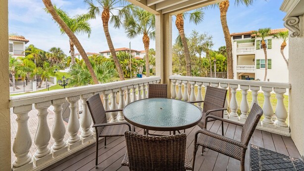 A covered outdoor area with a round table and wicker chairs, surrounded by a balustrade, overlooking a residential area with palm trees and houses. - Under the Tuscan Sun: *Heated Pool *Close to Beach *Perfect Central Location (Holmes Beach)