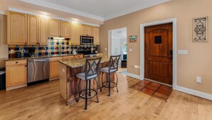 A kitchen with wooden cabinets, a microwave, and a tiled backsplash. There are two bar stools and a wooden door. - Under the Tuscan Sun: *Heated Pool *Close to Beach *Perfect Central Location (Holmes Beach)