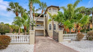 A two-story building with a balcony, surrounded by palm trees and a gravel driveway. - Under the Tuscan Sun: *Heated Pool *Close to Beach *Perfect Central Location (Holmes Beach)