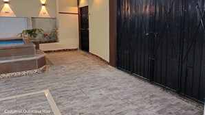 A covered outdoor area with a swimming pool, steps, and a black gate.