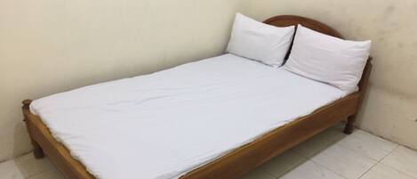 A single bed with a wooden frame and white bedding in a room with plain walls and tiled flooring.