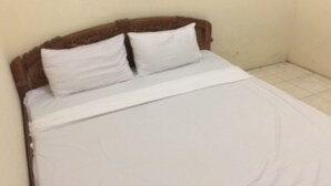 A single bed with a wooden headboard and white bedding in a room with plain walls and a tiled floor. - Hotel O Homestay Vicky 2 Syariah (Sidoarjo)