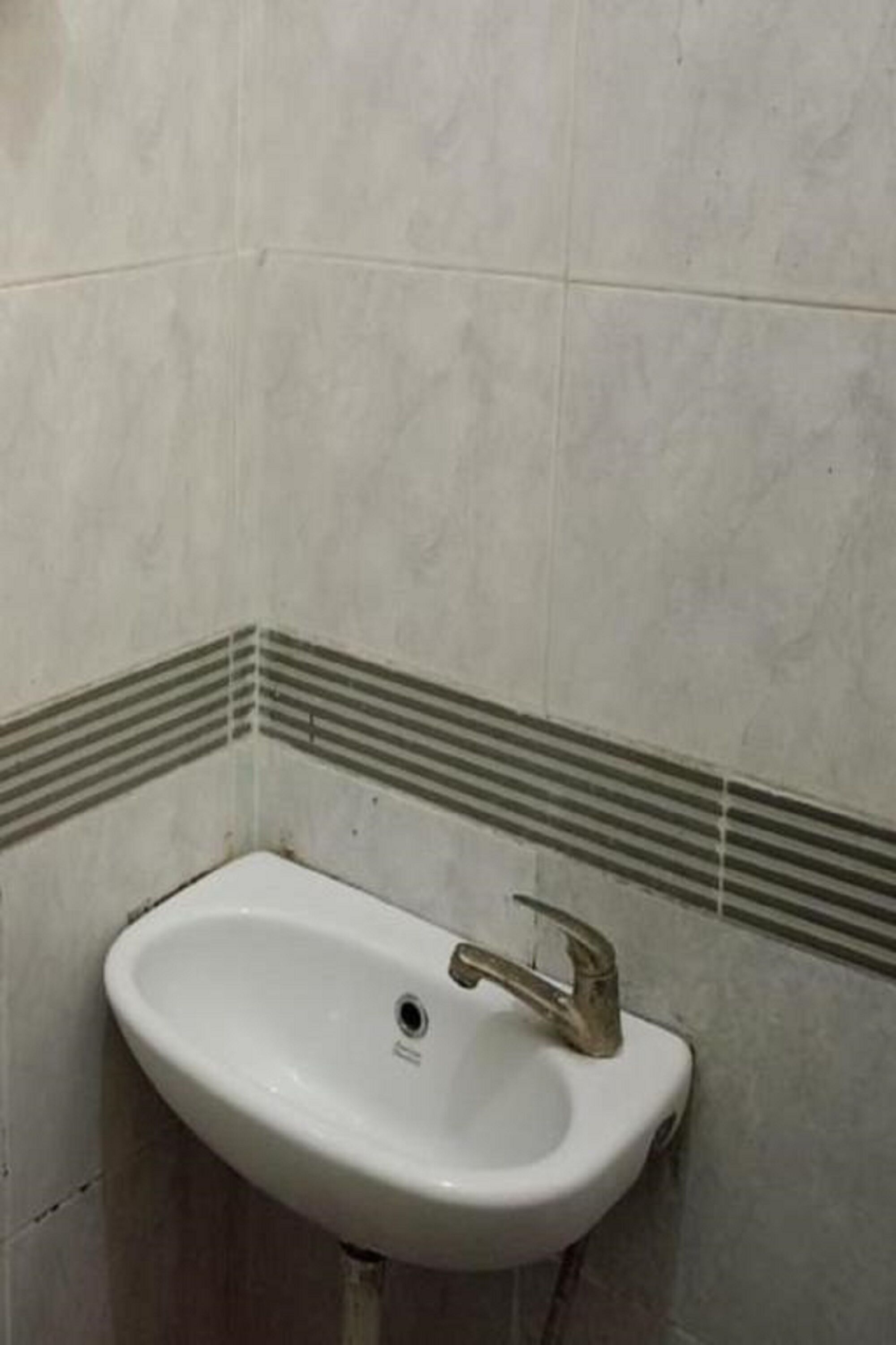 A white sink with a single faucet in a corner of a room with tiled walls.