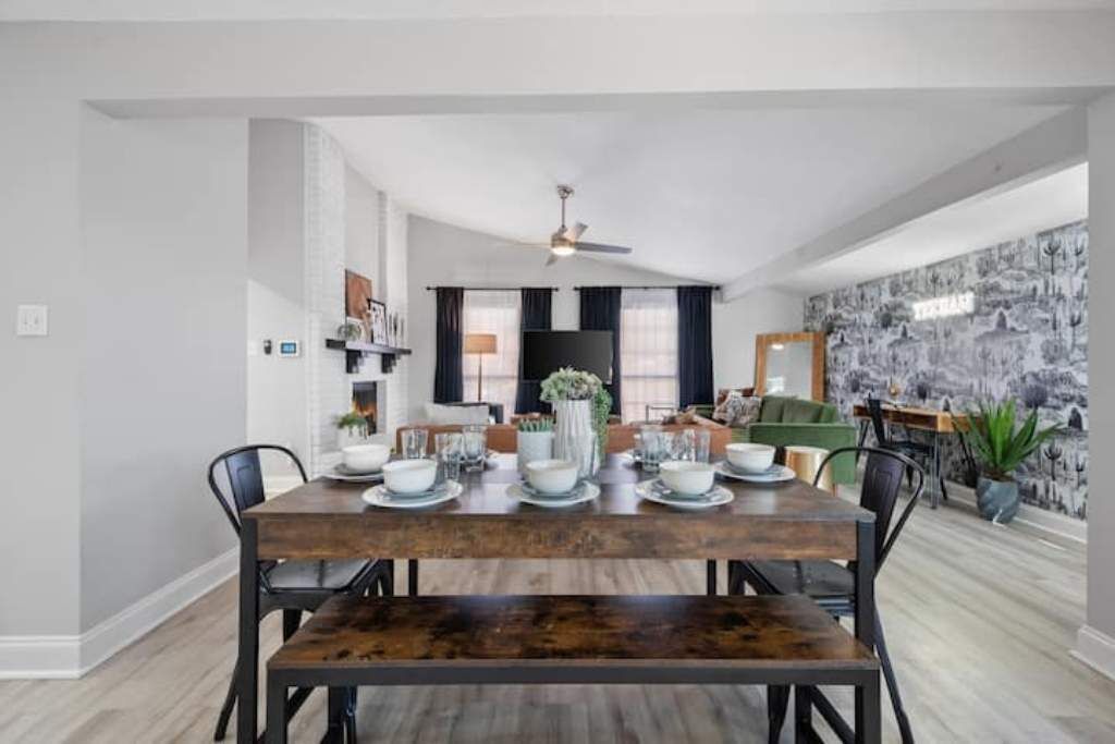 A dining area with a wooden table set for four, surrounded by black chairs. A ceiling fan is visible above the table.